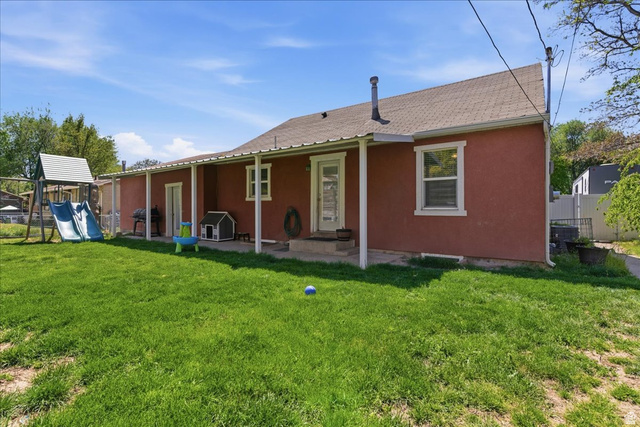 170 North 200 West Springville, UT 84663 - Photo 12 of 13 Expansive green lawn with a covered patio extending along the rear of the property, featuring a stucco exterior, multiple windows, and a back door access point