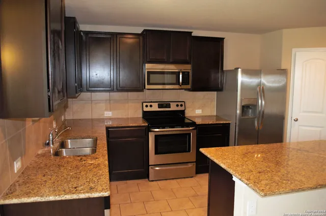 a kitchen with a granite counter tops a refrigerator and a stove top oven