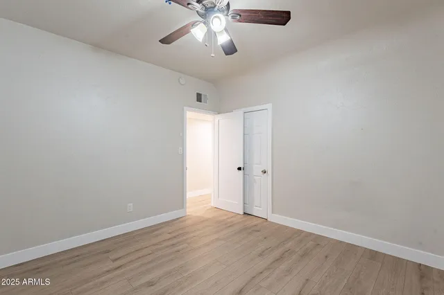 an empty room with wooden floor closet and fan