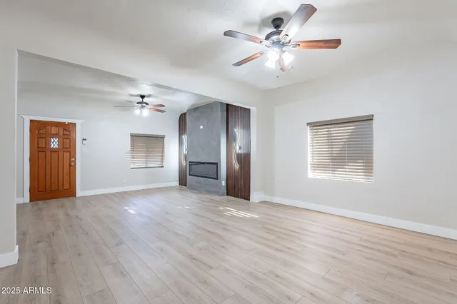 an empty room with wooden floor chandelier fan and windows