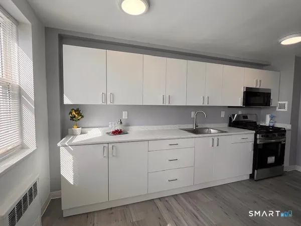 a kitchen with a sink dishwasher and white cabinets with wooden floor