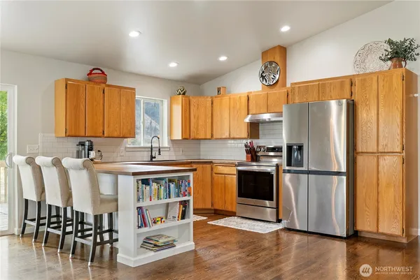 a kitchen with stainless steel appliances granite countertop a refrigerator a stove a sink a dining table and chairs with wooden floor