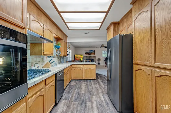 a large kitchen with stainless steel appliances granite countertop a refrigerator a sink dishwasher and wooden cabinets with wooden floor