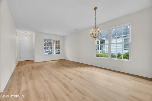 an empty room with wooden floor chandelier and windows