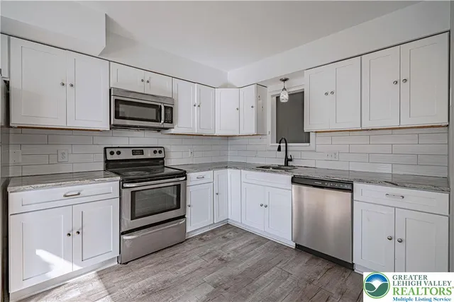 a kitchen with stainless steel appliances granite countertop white cabinets a sink a stove a microwave and cabinetry