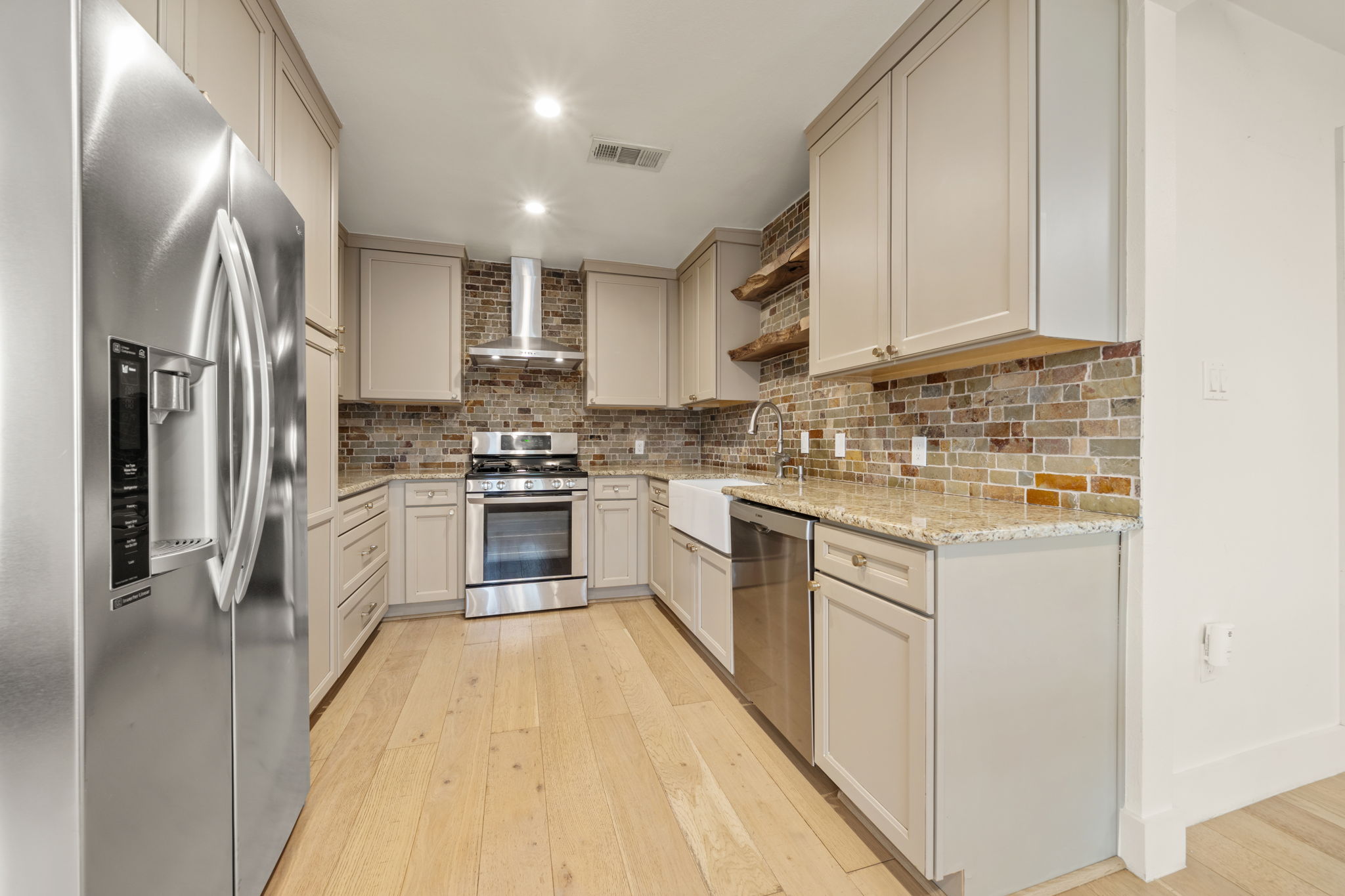 912 Mansell Avenue Austin, TX 78702 - Photo 13 of 37 Kitchen featuring stainless steel appliances, light stone countertops, open shelves, wall chimney exhaust hood, and light wood-style floors