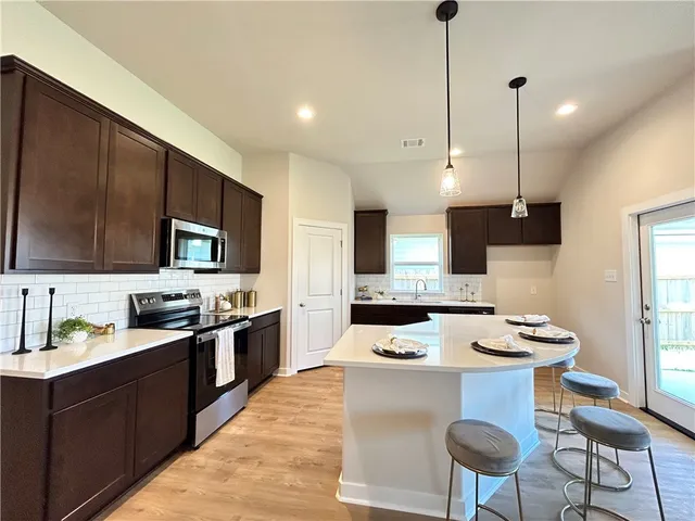 a kitchen with stainless steel appliances a stove top oven a sink a refrigerator and chairs