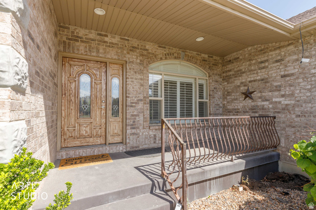 2327 Bluff Ridge Drive Syracuse, UT 84075 - Photo 6 of 66 Brick exterior with a covered porch featuring a decorative wood-paneled door with glass inserts, an arched window with plantation shutters, and an ornate metal railing