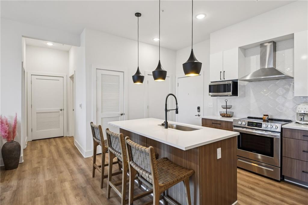 112 Rogers Street Northeast, Unit 409 Atlanta, GA 30317 - Photo 4 of 18 a kitchen with stainless steel appliances a stove a sink a oven a dining table and chairs with wooden floor