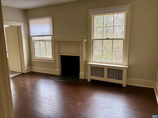 an empty room with wooden floor fireplace and windows