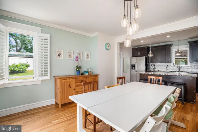 a room with stainless steel appliances kitchen island granite countertop a refrigerator a sink dishwasher a dining table and chairs with wooden floor