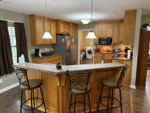 a kitchen with stainless steel appliances kitchen island granite countertop a table chairs and a refrigerator