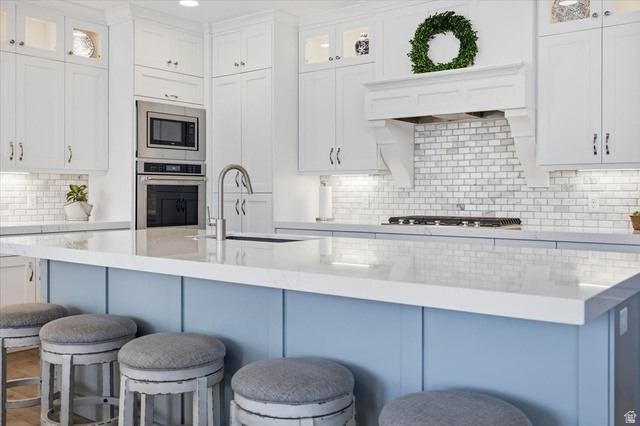 21 Pier Place Tooele, UT 84074 - Photo 25 of 112 Kitchen featuring a light blue island with a white countertop, subway tile backsplash, white shaker cabinetry, stainless steel built-in appliances, and recessed lighting