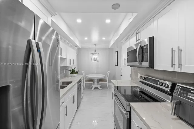 a kitchen with stainless steel appliances granite countertop a refrigerator a stove a sink a microwave oven with white cabinets and wooden floor