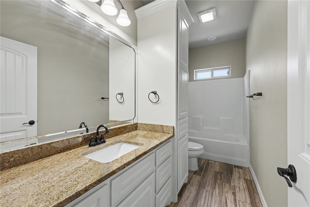 302 Cooper Road, Unit E2 Odem, TX 78370 - Photo 16 of 24 a bathroom with a granite countertop sink a toilet a mirror and shower