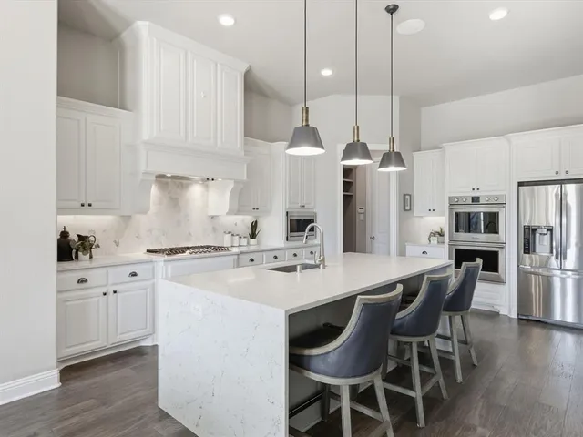 a kitchen with stainless steel appliances kitchen island granite countertop a table chairs stove and white cabinets