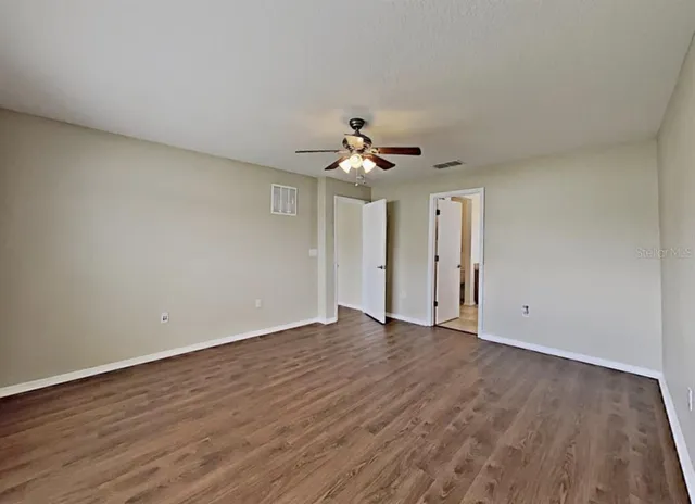 a view of an empty room with wooden floor and a ceiling fan