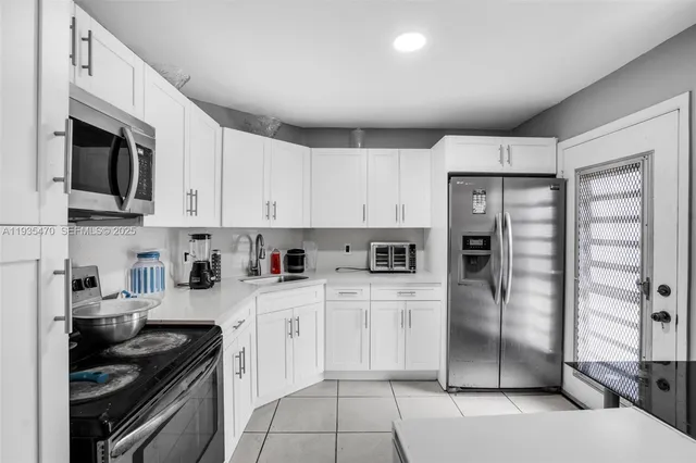 a kitchen with stainless steel appliances granite countertop a refrigerator a stove a sink and white cabinets