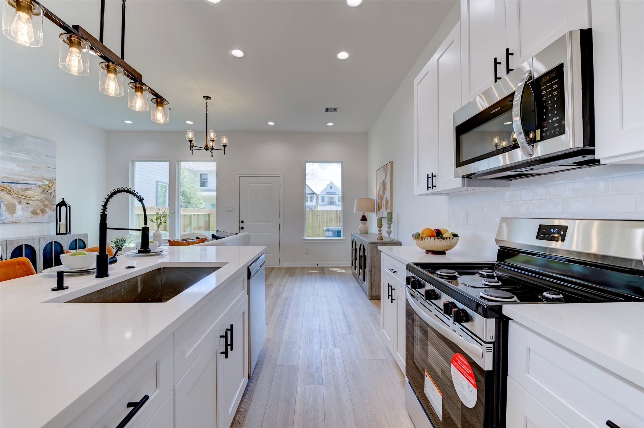6807 Paris Street Houston, TX 77021 - Photo 19 of 50 Full kitchen showing white shaker cabinets with matte black hardware, quartz countertops, subway tile backsplash, stainless appliances including range, microwave, and dishwasher, farmhouse sink, and Edison pendant rail lighting.