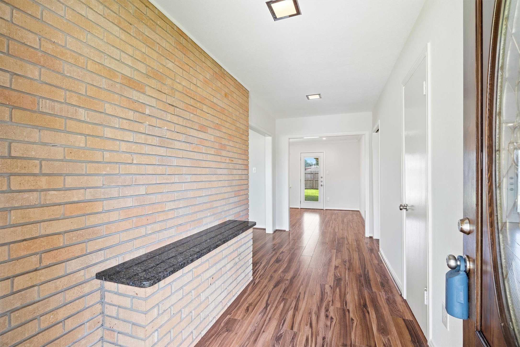 3331 Arbor Street Houston, TX 77004 - Photo 3 of 30 This entryway features a stylish brick accent wall and rich wooden flooring, leading to a bright doorway with a view of the backyard.