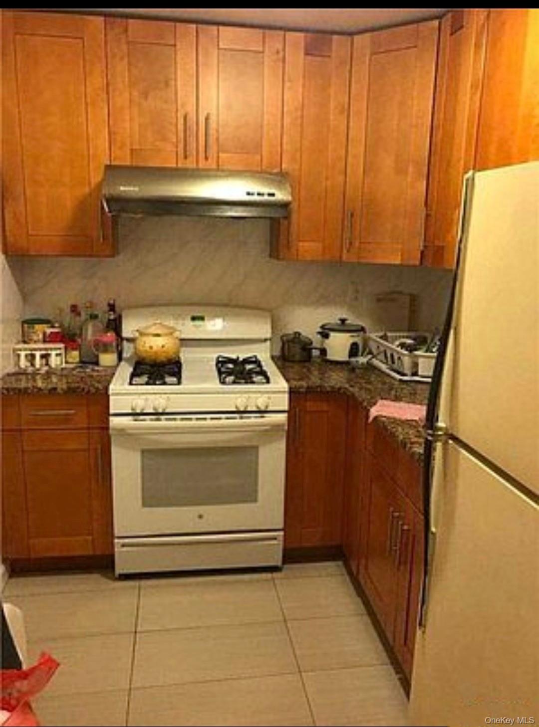 132-35 Sanford Avenue, Unit LD Queens, NY 11355 - Photo 6 of 9 Kitchen featuring white appliances, light tile patterned flooring, brown cabinets, and under cabinet range hood
