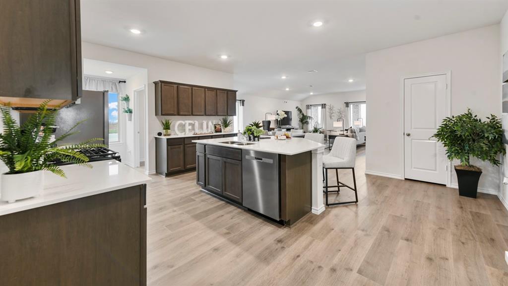 1671 Mantle Road Crandall, TX 75114 - Photo 3 of 24 Spacious kitchen featuring an expansive center island with a stainless steel dishwasher, wood-finish cabinetry, light-toned countertops, a built-in oven, and wood-finish flooring