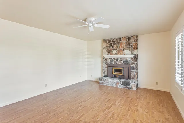 a view of a livingroom with a fireplace a ceiling fan and wooden floor