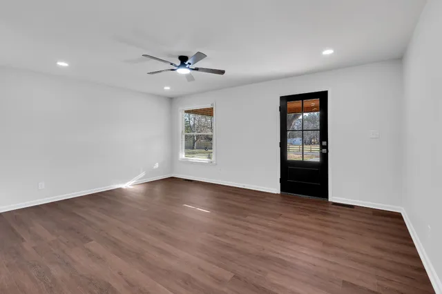 a view of an empty room with wooden floor and a ceiling fan