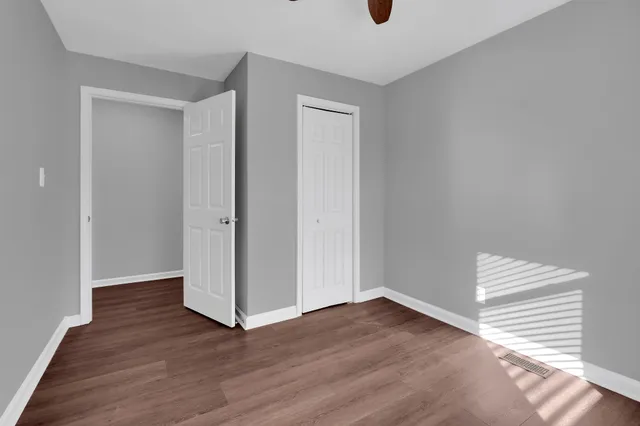 an empty room with wooden floor ceiling fan and windows