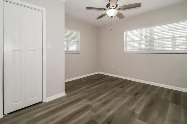an empty room with wooden floor chandelier fan and windows