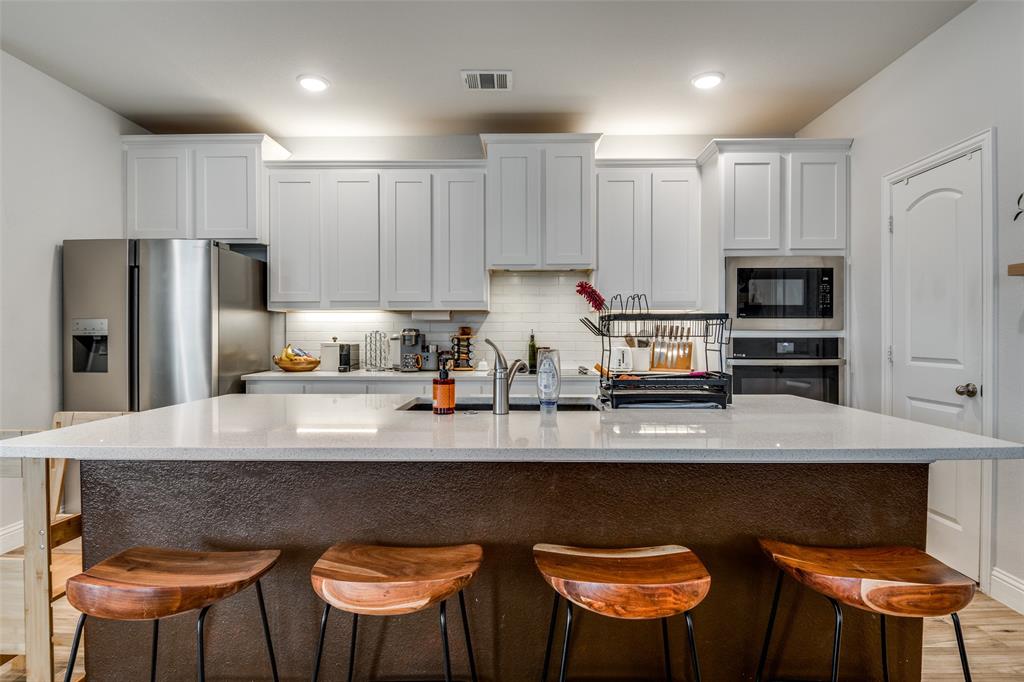 8413 Alba Lane Rowlett, TX 75089 - Photo 10 of 25 Kitchen with light wood-style flooring, white cabinetry, decorative backsplash, a kitchen breakfast bar, and stainless steel appliances