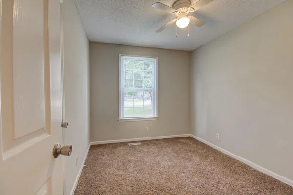 an empty room with a chandelier fan and windows