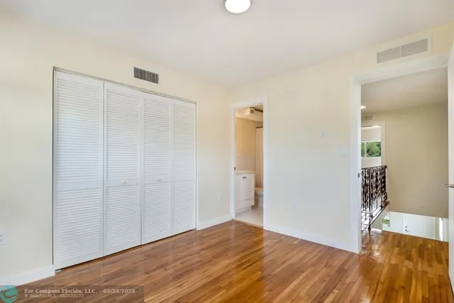 a view of an empty room with wooden floor and a bathroom
