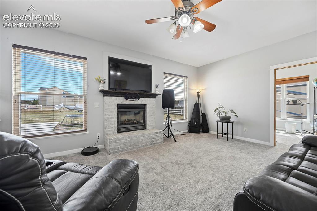 8347 Tibbs Road Peyton, CO 80831 - Photo 3 of 39 Living space featuring a light gray brick fireplace with a dark mantel, a ceiling fan with integrated lighting, and light gray wall paint