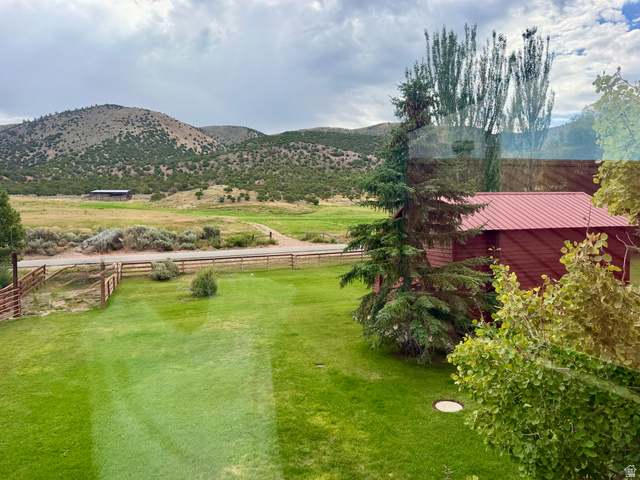 1825 North Cisco Road Laketown, UT 84038 - Photo 29 of 34 Expansive green lawn, fenced perimeter, distant mountainous terrain, red siding structure with metal roof, mature trees