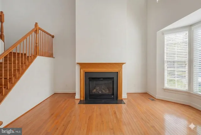 a view of an empty room with wooden floor fireplace and a window