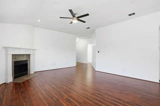 an empty room with wooden floor a ceiling fan and fireplace