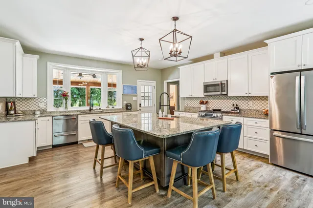 a kitchen with stainless steel appliances a dining table chairs refrigerator and cabinets