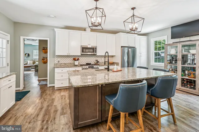 a kitchen with stainless steel appliances granite countertop a stove top oven a refrigerator a sink dishwasher a dining table and chairs with wooden floor