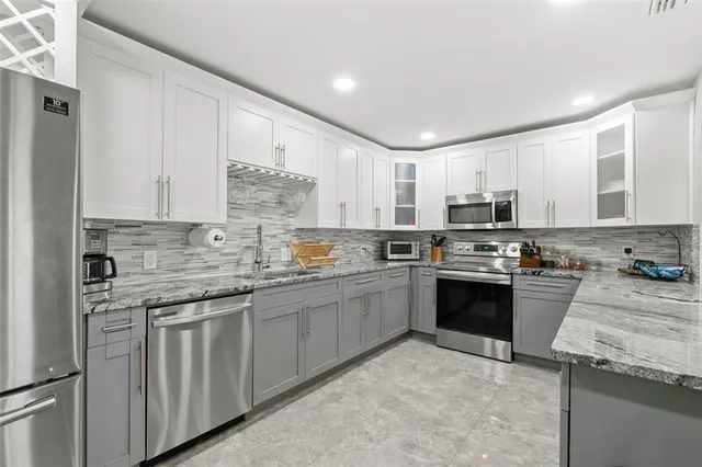 a kitchen with stainless steel appliances granite countertop a stove top oven a sink and dishwasher a refrigerator with white cabinets