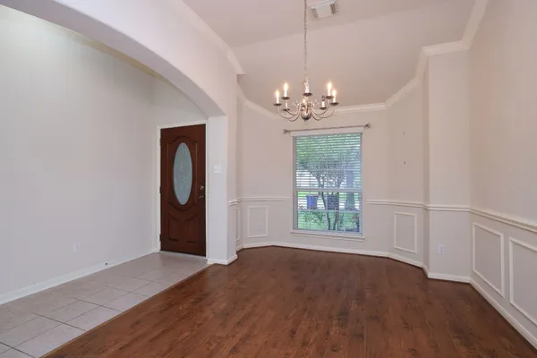 an empty room with wooden floor chandelier and windows