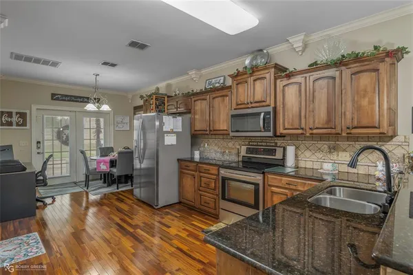 a kitchen with stainless steel appliances granite countertop wooden cabinets a sink dishwasher a stove and a microwave oven with wooden floor