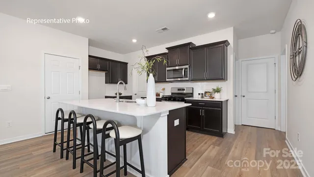 a kitchen with stainless steel appliances granite countertop a sink a stove a refrigerator and a microwave with wooden floor