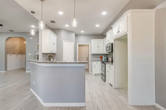 a large kitchen with a large counter top a sink stainless steel appliances and cabinets