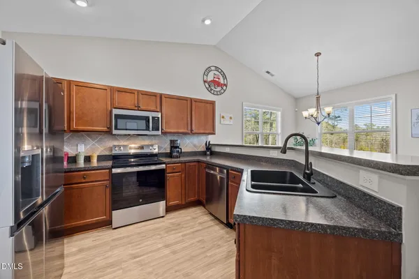 a kitchen with stainless steel appliances granite countertop a refrigerator sink and wooden cabinets