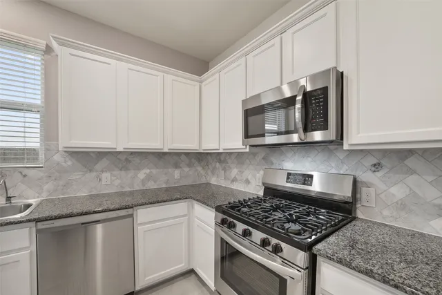 a kitchen with stainless steel appliances granite countertop white cabinets granite counter tops and a wooden floors