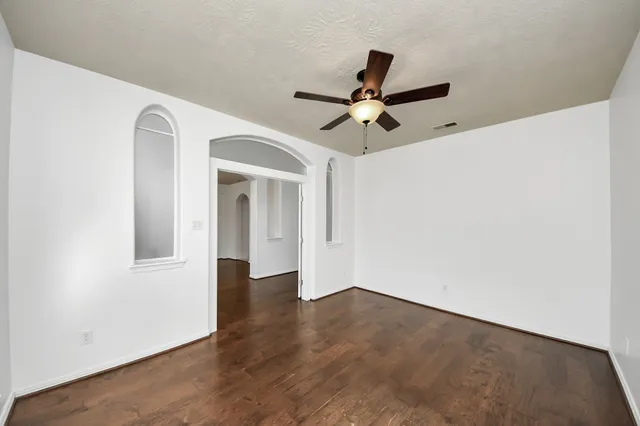 an empty room with wooden floor ceiling fan and windows