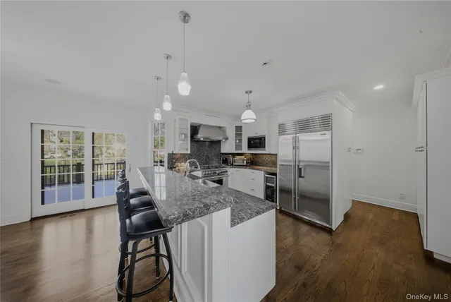 a kitchen with stainless steel appliances kitchen island granite countertop a refrigerator a stove top oven a sink island and a wooden floor