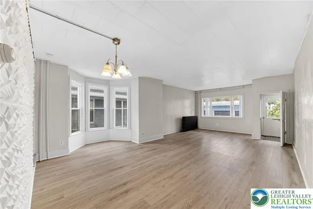 an empty room with wooden floor chandelier and windows