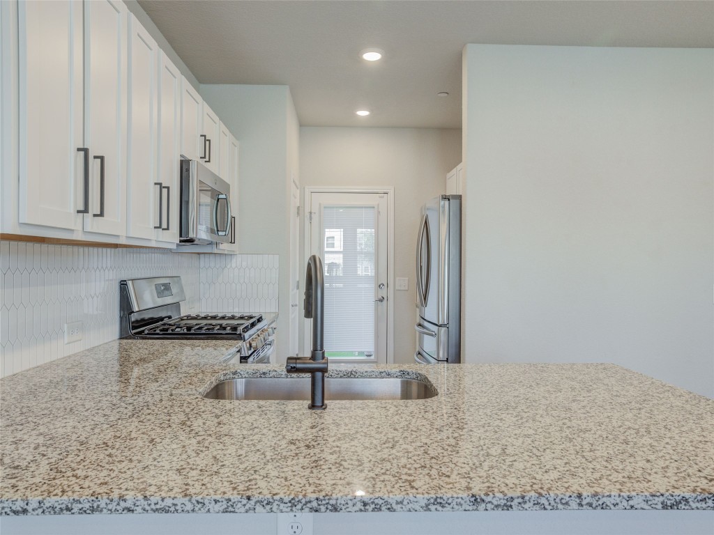 9015 Cattle Baron Path, Unit 502 Austin, TX 78747 - Photo 9 of 40 Kitchen with a peninsula, light stone counters, stainless steel appliances, white cabinets, and tasteful backsplash